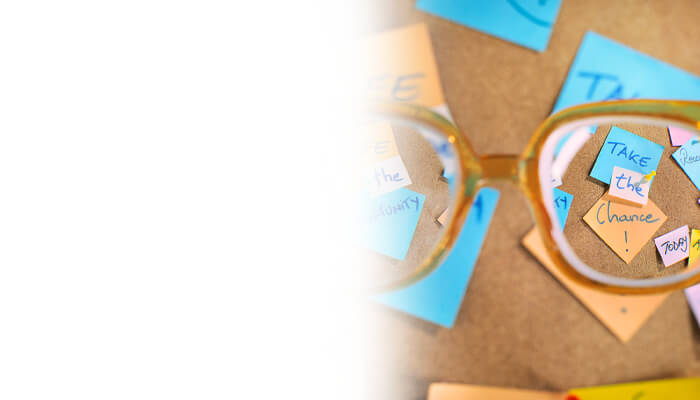 Glasses rest in front of a corkboard filled with colorful sticky notes, featuring motivational messages